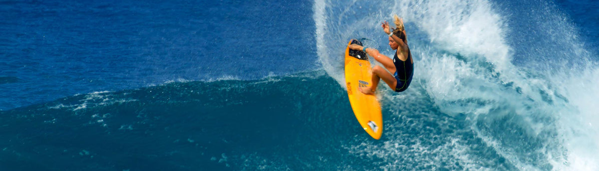 Coco Ho, Team NORTH Athlete, rides a massive wave on a yellow surfboard