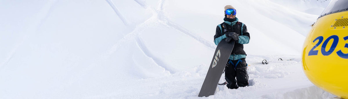 Travis Rice, Team NORTH Athlete, standing with his snowboard in the snow