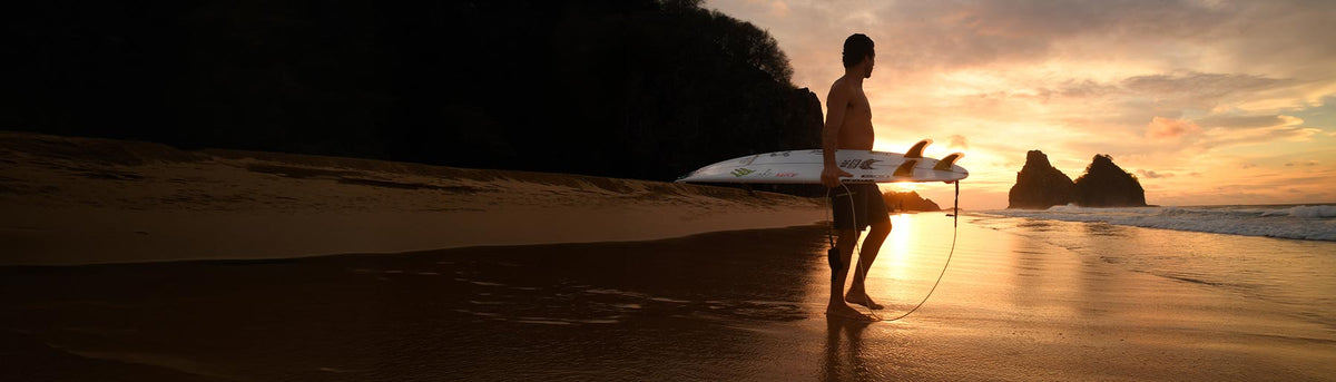 Yago Dora, Team NORTH Athlete, stands on a beach at sunset, looking out at the waves