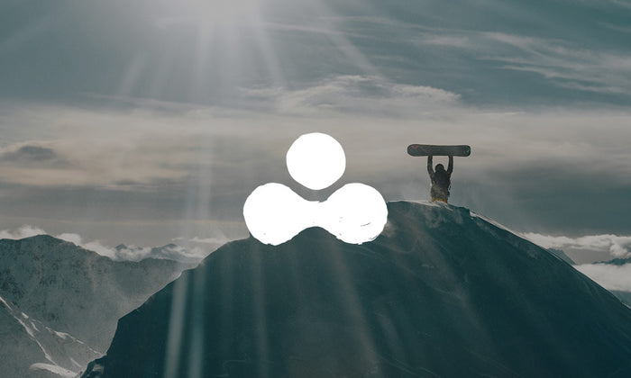 Photo of a snowboarder holding their board up in celebration at the top of a snowy mountain. There is an icon on top of the image.