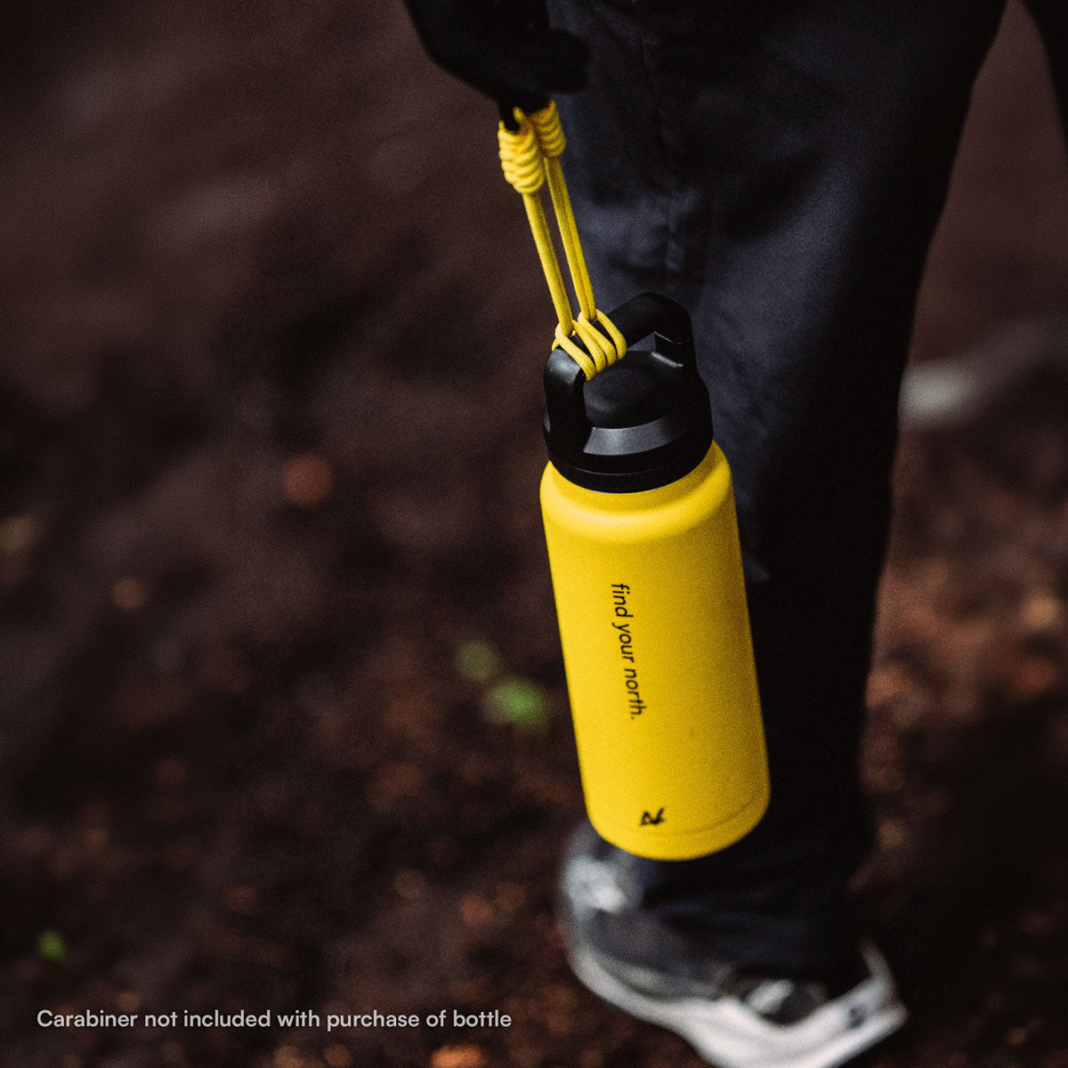 A close-up of a person outdoors holding a bright yellow bottle with a black cap and yellow loop strap. The bottle has the words 'find your north.