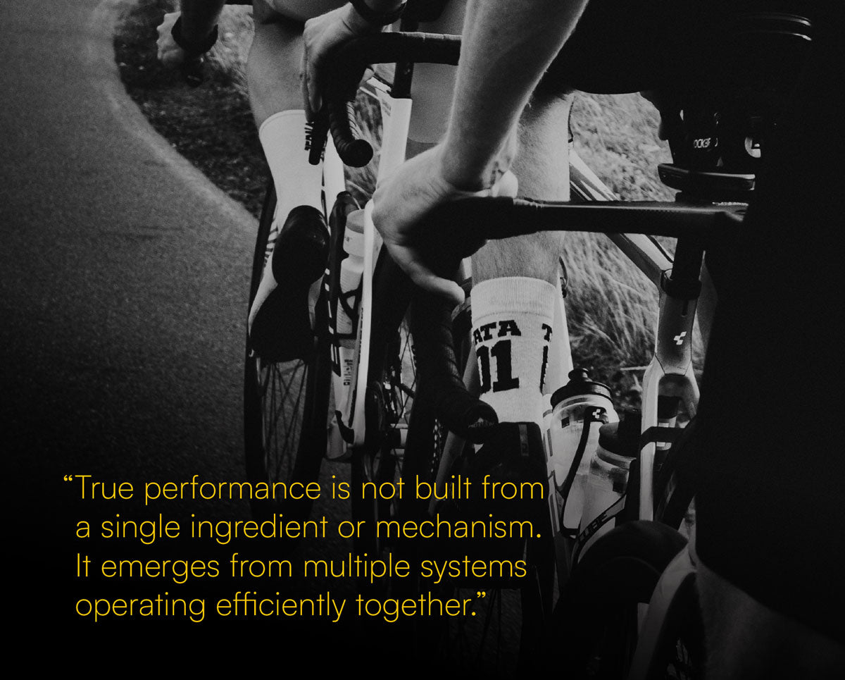 Black and white close-up photo of a cyclist riding a bicycle on a road, with a yellow quote overlaid at the bottom left: 'True performance is not built from a single ingredient or mechanism. It emerges from multiple systems operating efficiently together.